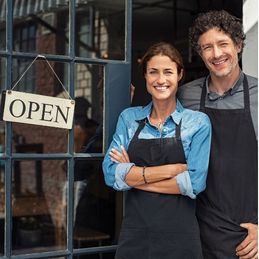 man and woman standing in front of their business with an open sign hanging on the door